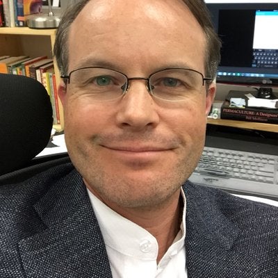 Greg smiling in suit at desk