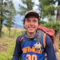 Portrait of Max smiling outdoors with a cap and hiking backpack