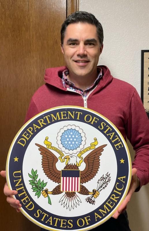 Portrait of Nathan holding Department of State seal and smiling