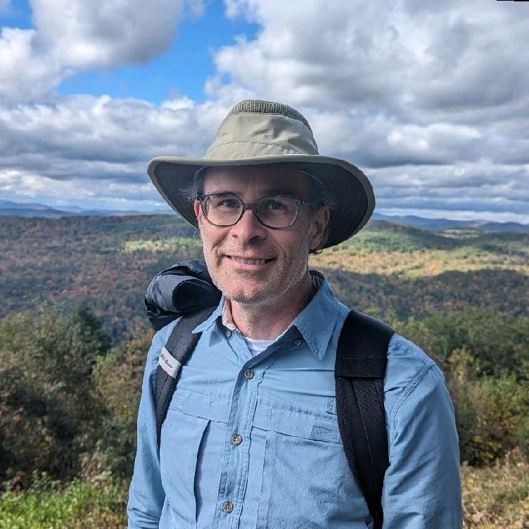 Portrait of Brent in hiking gear, smiling in front of a mountain landscape